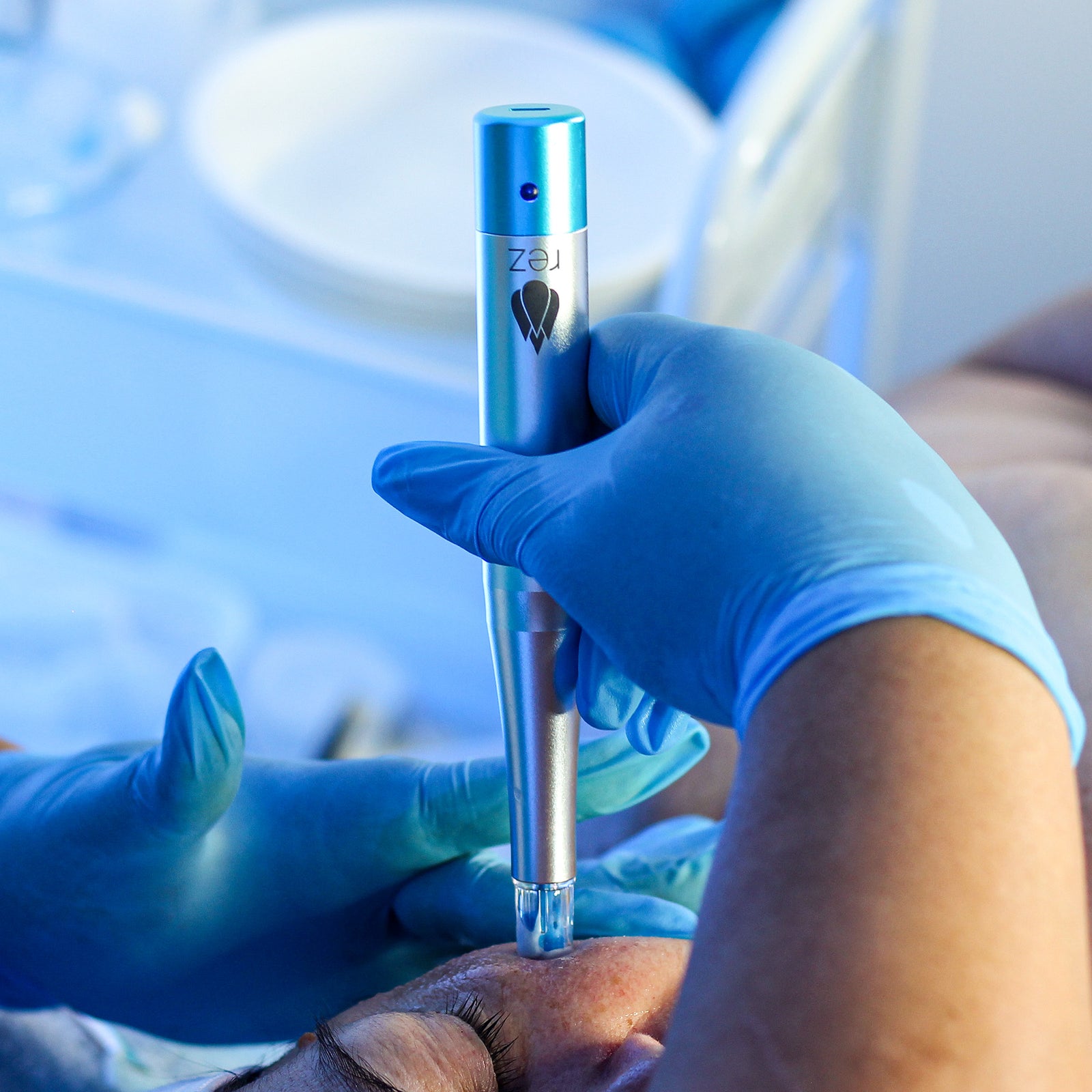 Person wearing blue gloves holding a Rezenerate device on a blurred background