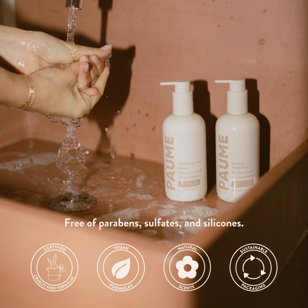 Two bottles of PAUME skincare products on a sink with hands washing under running water.
