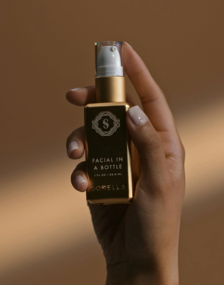 A hand holding a gold serum bottle 